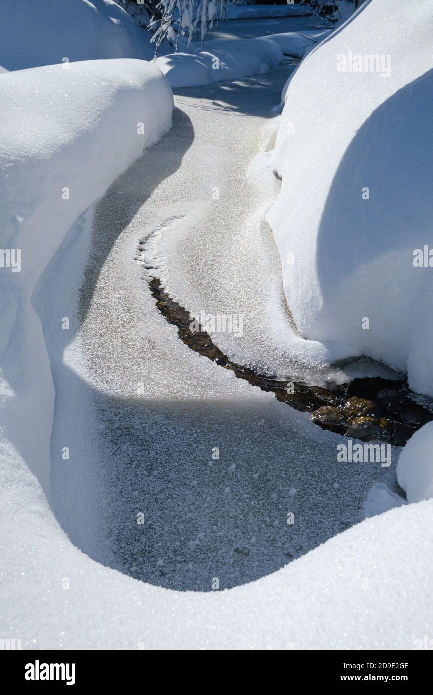 Kleiner gefrorener Bach mit Schneeverwehungen an den Ufern in schneebedeckten Bergen Winterwald Stockfoto