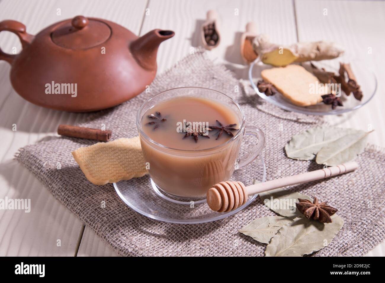 Masala Tee-Indischer belebender Tee mit Milch und Gewürzen auf weißem Hintergrund mit einer Serviette in einer Glas-Tasse und einer Keramik-Teekanne. Horizontal Stockfoto