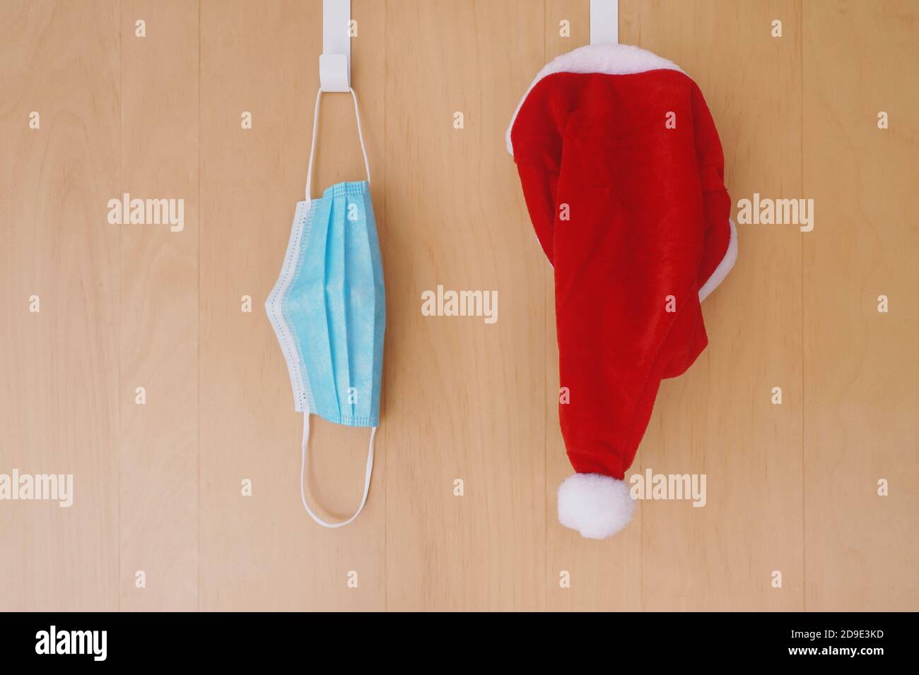 Gesichtsmaske und weihnachtsmann Hut hängen Seite an Seite An den Türhaken - weihnachten während der Corona-Pandemie covid-19 Stockfoto