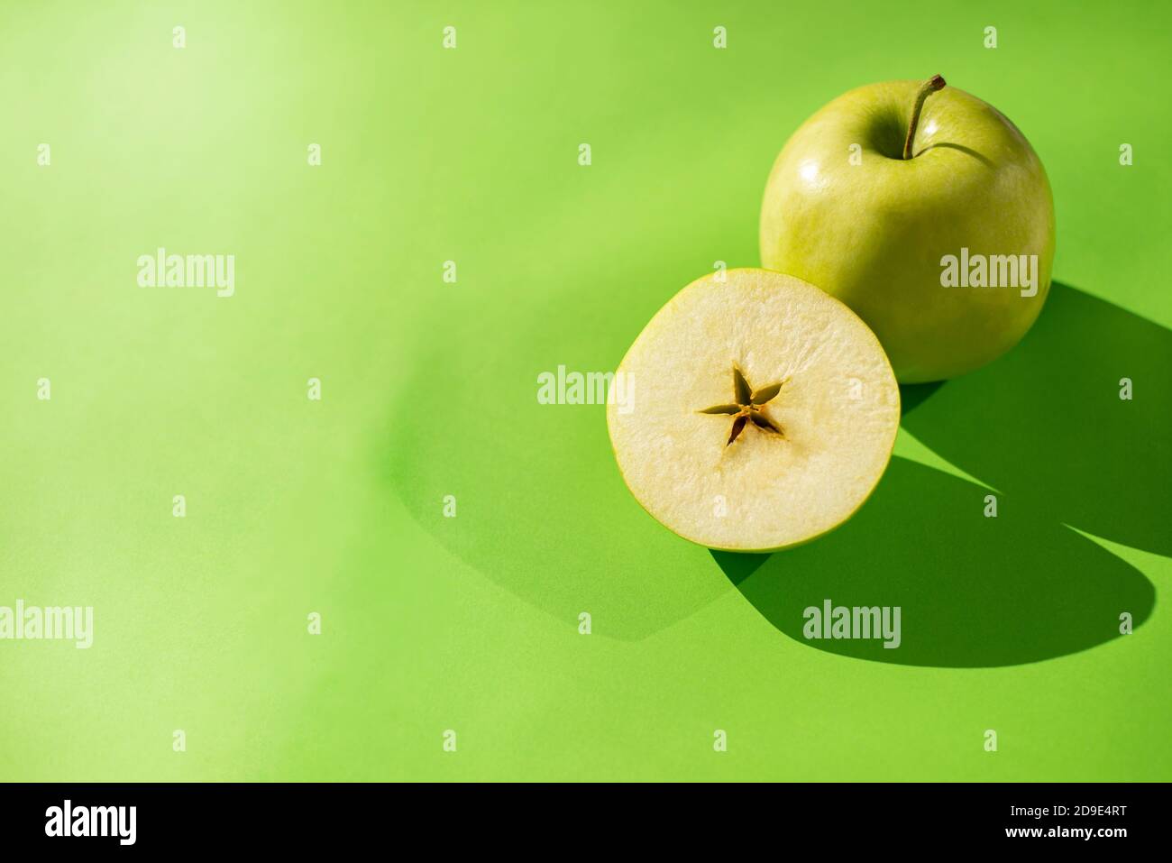 Grüner Apfel ganz und schneiden Sie die Hälfte auf einem grünen Hintergrund. Sternförmiger Apfelkern. Schatten von Äpfeln. Platz für Text kopieren. Stockfoto