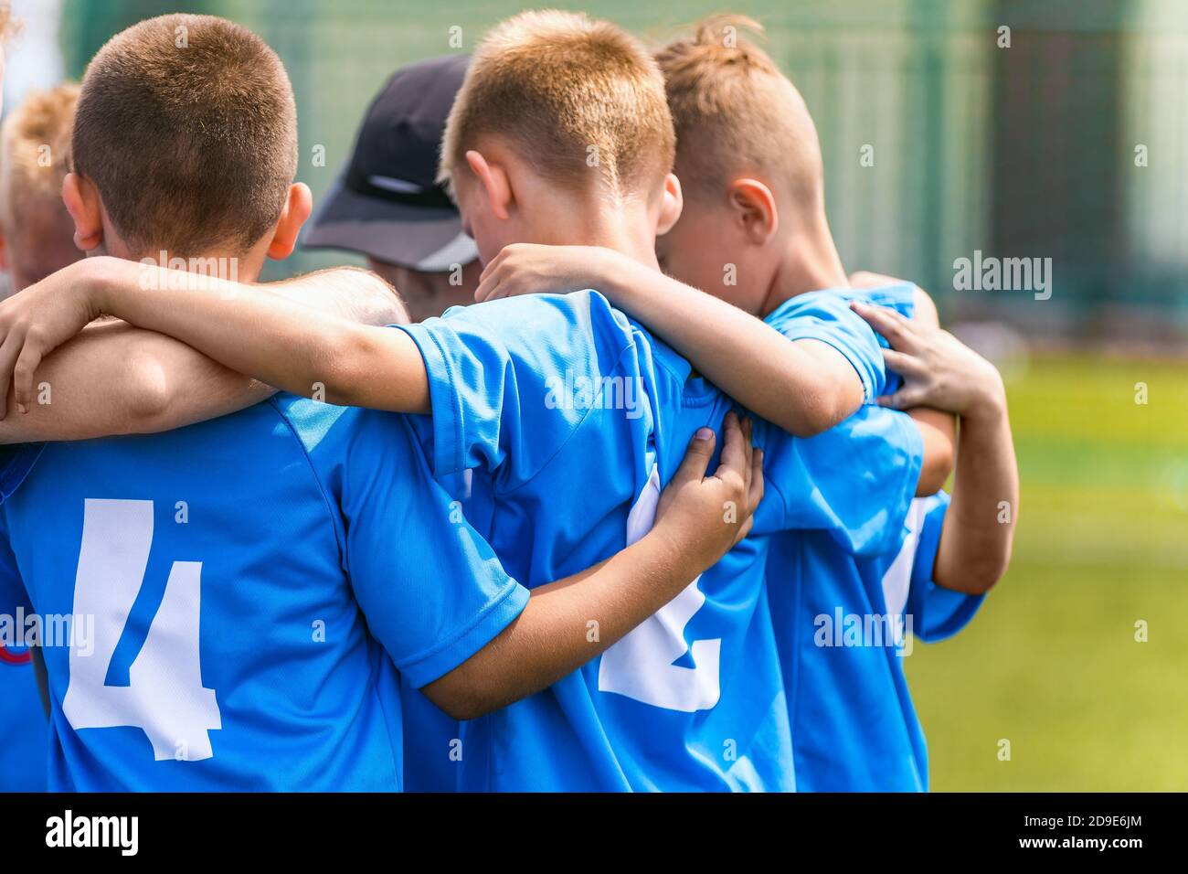 Kinder Fußballmannschaft mit Trainer in der Gruppe huddle vor dem Spiel. Kinder im Grundschulalter hören gemeinsam zu, um motivierende Reden zu coachen. Jungen in blu Stockfoto