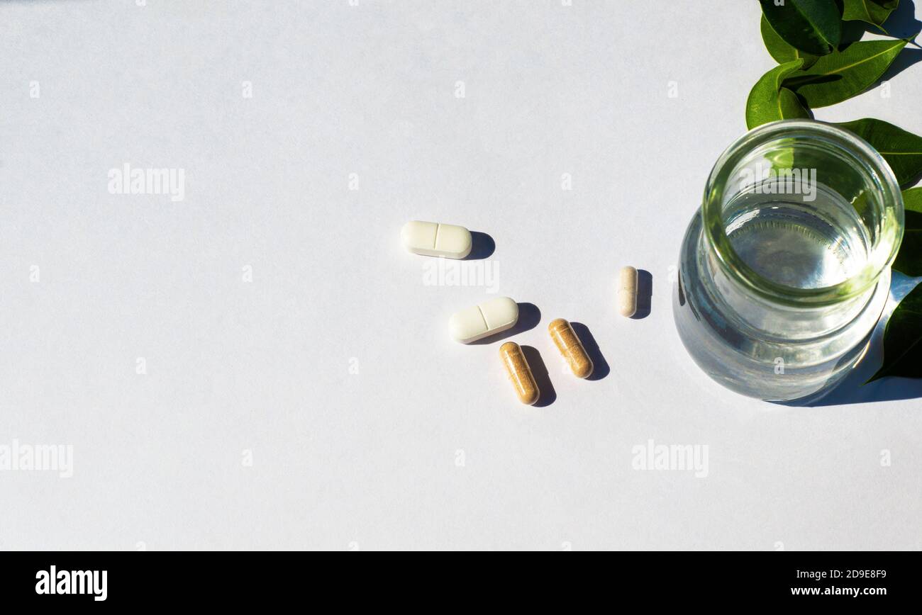 Glasbecher mit Wasser und Kapseln und Pilli auf weißem Hintergrund. Das Thema der nutrazeutischen Medizin und die Einnahme von biologischen Nahrungsergänzungsmitteln. Stockfoto