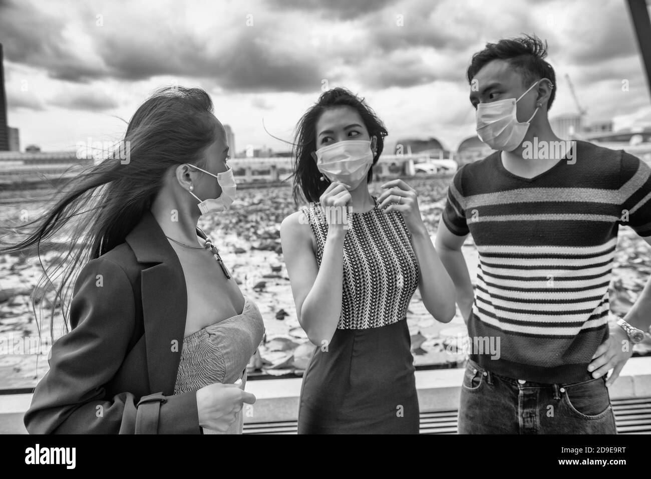 Drei glücklich junge asiatische Freunde im Freien tragen Gesichtsmaske in Covid Pandemie Prävention Stockfoto
