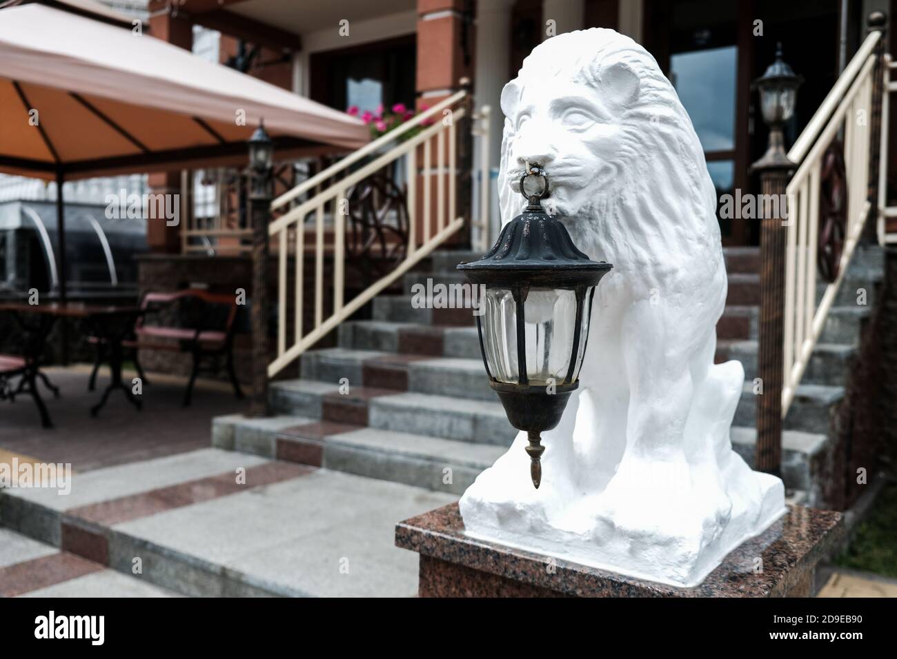 Weiße Löwenstatue mit einer alten Laterne vor einer Hotel- oder Restaurantfassade. Treppe im Hintergrund. Hospitality-Konzept. Sightseeing im Osten Stockfoto