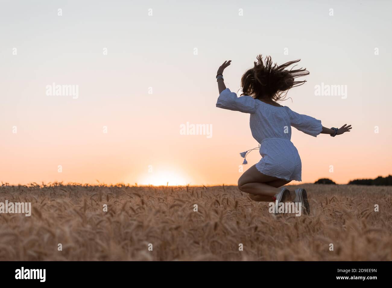 Eine junge Frau zu fangen, die während des Sonnenuntergangs über das Getreidefeld springt Stockfoto