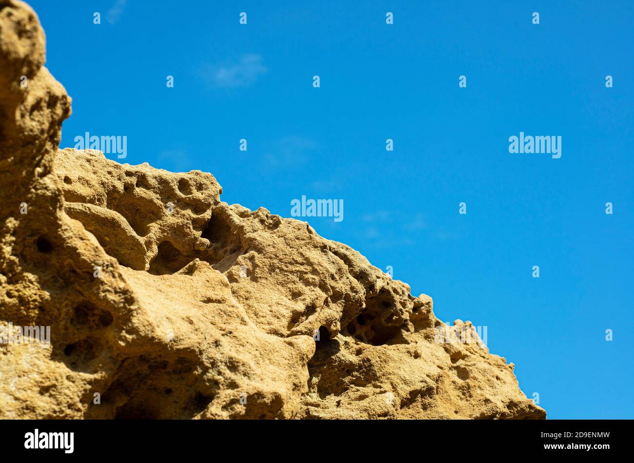 Felsstruktur auf einem Hintergrund von blauem Himmel. Die poröse perforierte Textur des Steins. Küstenfelsen. Stockfoto