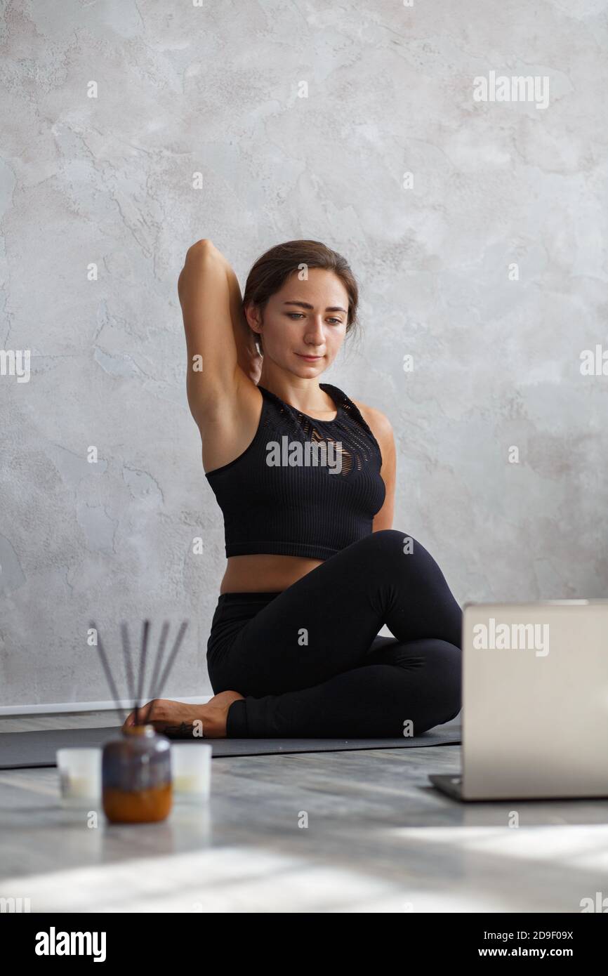 Junge sportliche Frau, die Online-Yoga-Unterricht auf Laptop. Schönes Mädchen üben Kuh Gesicht Pose, gomukhasana. Yoga-Haltungen, Meditation, Entspannung Stockfoto