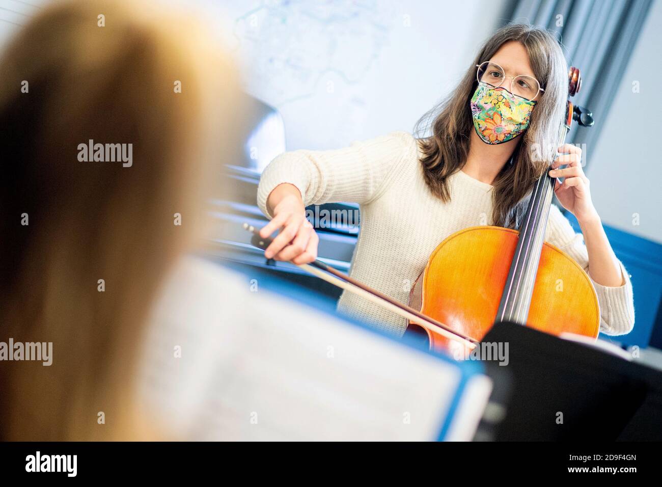 Hannover, Deutschland. November 2020. Musikpädagogin Sophia Grest spielt ihr Cello während eines Unterrichts an der städtischen Musikschule, mit einem Mund-und-Nase-Cover. Die mehr als 70 öffentlichen und gemeinnützigen Musikschulen Niedersachsens können aufgrund ihrer Einstufung als Bildungseinrichtungen trotz der teilweisen Sperrung im November weiterhin geöffnet bleiben. Beim Musizieren müssen Lehrer und Schüler eine Mundschutz tragen. Quelle: Hauke-Christian Dittrich/dpa/Alamy Live News Stockfoto