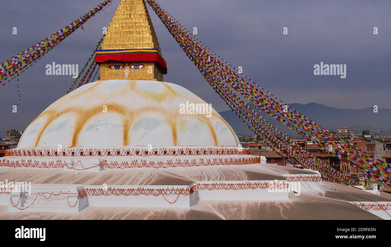 Riesige Boudhanath Stupa (Boudha) im Zentrum von Kathmandu, Nepal mit bunten buddhistischen Gebetsfahnen und Blumenfestoons mit Gebäuden geschmückt. Stockfoto