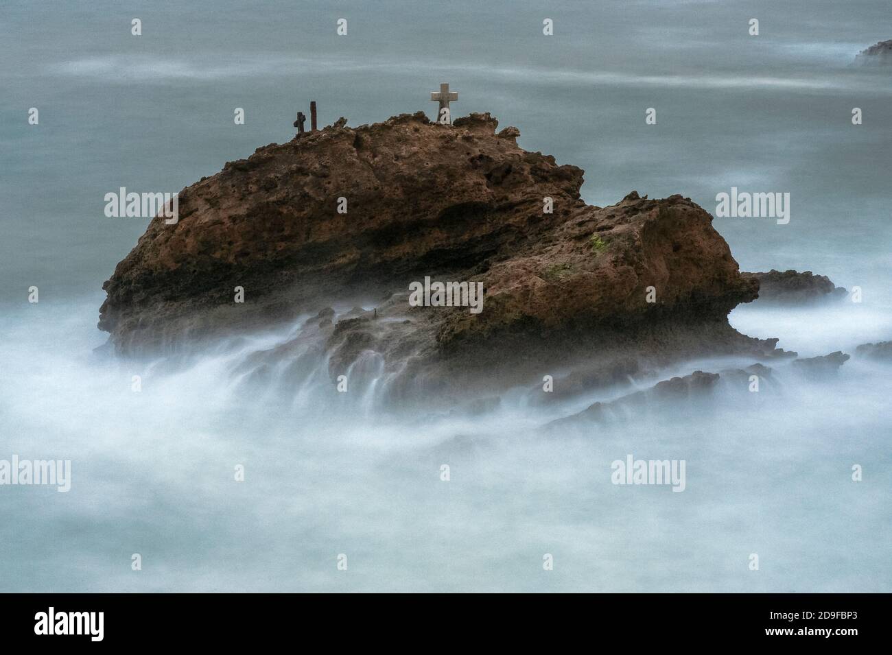 La Roche Battue (der zerschlagene oder geschlagene Felsen), der bei Flut nicht weit in die stürmische Bucht von Biscay vor dem Grand Plage Strand in Biarritz, Nouvelle-Aquitaine, Frankreich, liegt. Sie trägt ein beschriftete Kreuz und andere Gedenkstätten an die ertrunkene fünfköpfige Besatzung der Schlinge ‘La Surprise’, die in rauschenden Meeren Segel und Ruder verlor, während sie Schiefer von Bayonne nach London, England, transportete. Das Schiff lief am nächsten Tag, dem 17. November 1893, auf La Roche Battue, auch bekannt als l’Arroque Trudade, auf Grund. Ein Mann wurde tot aufgefunden, aber die Leichen der anderen vier wurden nie geborgen. Stockfoto