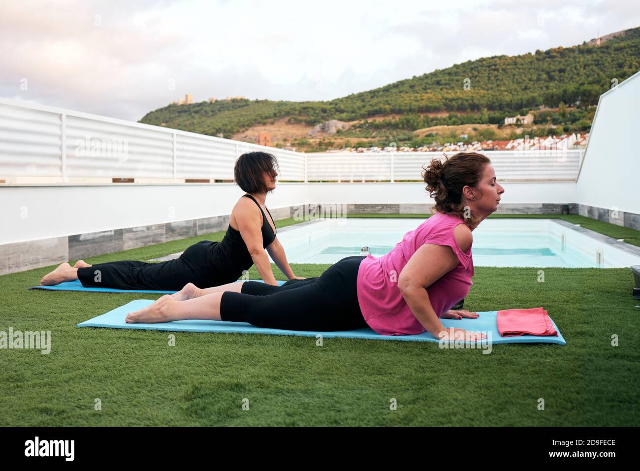 Zwei Frauen üben Yoga auf der Terrasse des Hauses Halbe Kobra-Haltung Stockfoto
