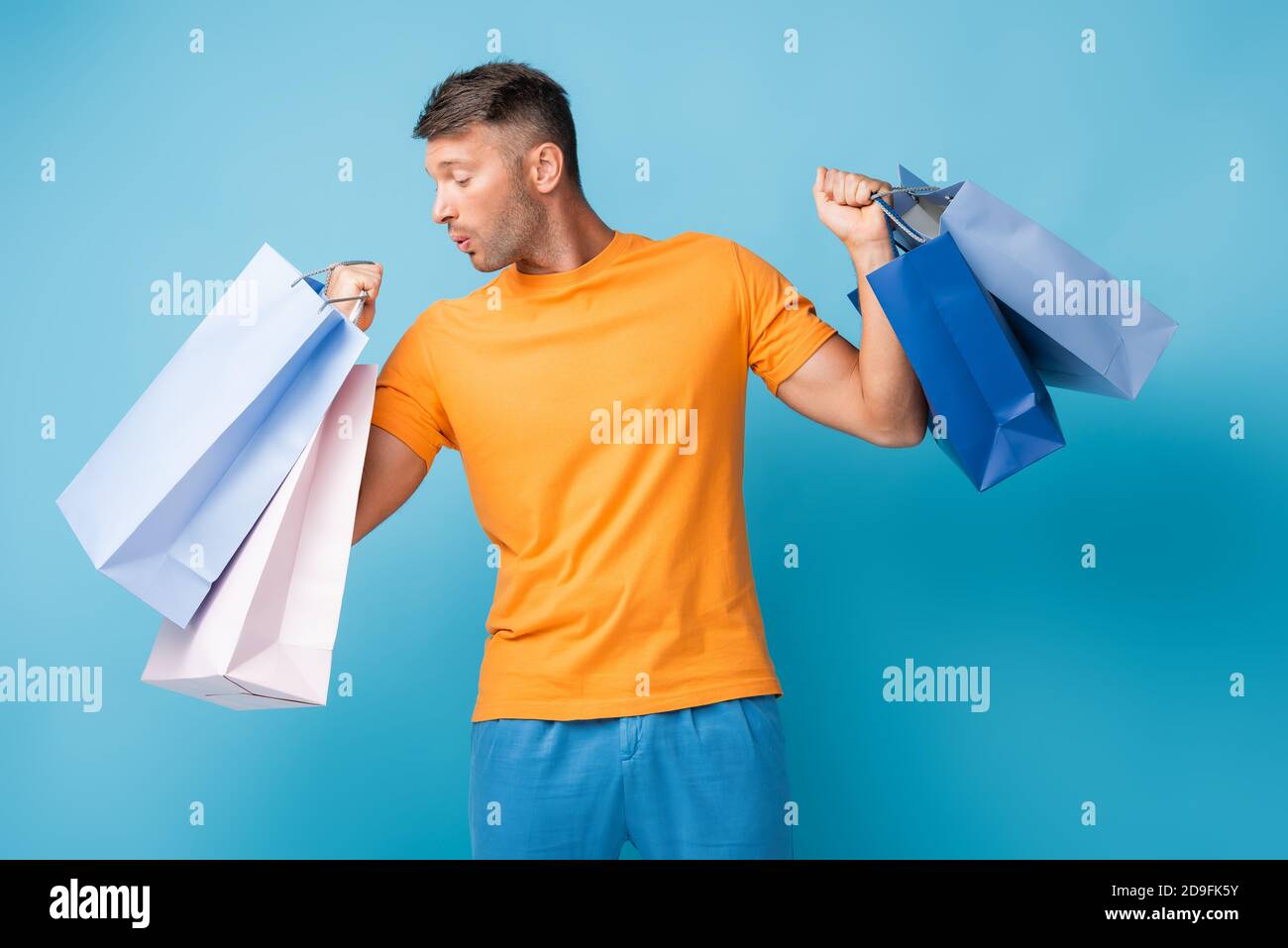 Überrascht Mann in T-Shirt hält Einkaufstaschen auf blau Stockfoto