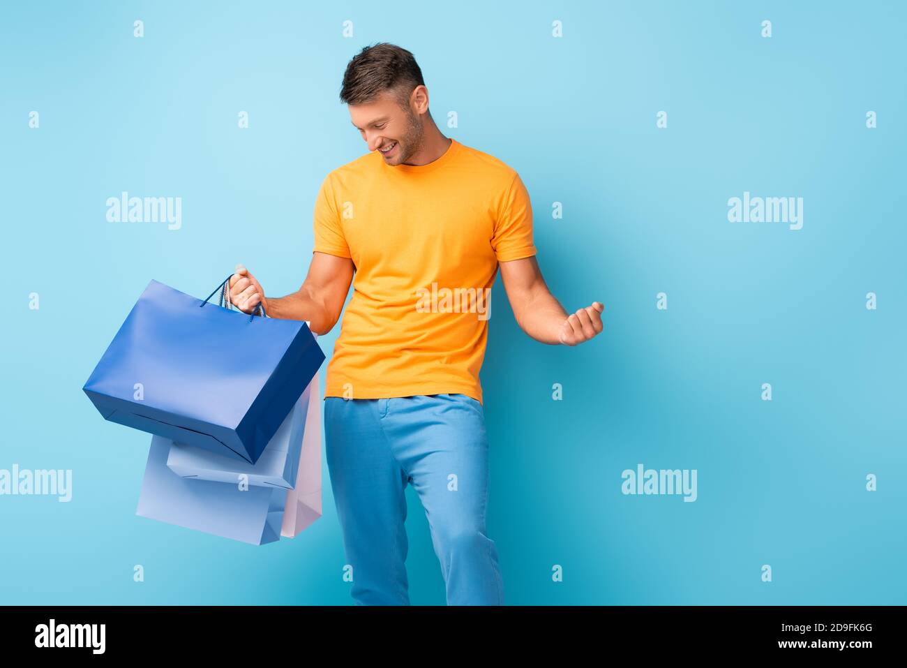 Glücklicher Mann in T-Shirt hält Einkaufstaschen auf blau Stockfoto