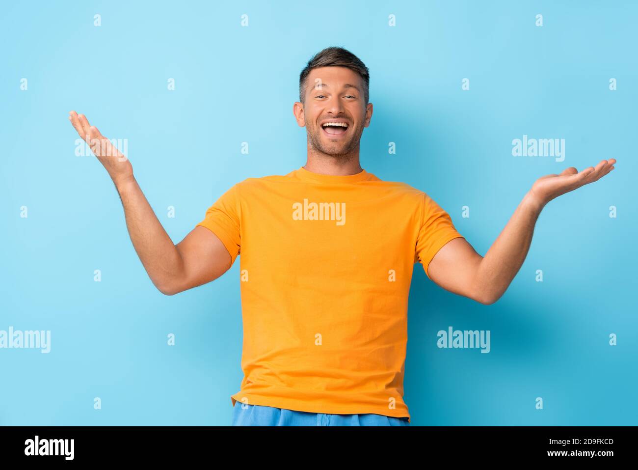 Aufgeregter Mann in gelbem T-Shirt gestikuliert auf blau Stockfoto