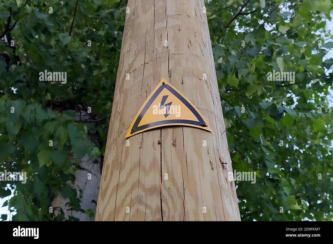 Zeichen der Gefahr eines elektrischen Schlags auf einem Holzmast. Schwarzer Blitz gegen ein gelbes Dreieck. Stock Foto mit leerem Platz für Text und Design. Stockfoto