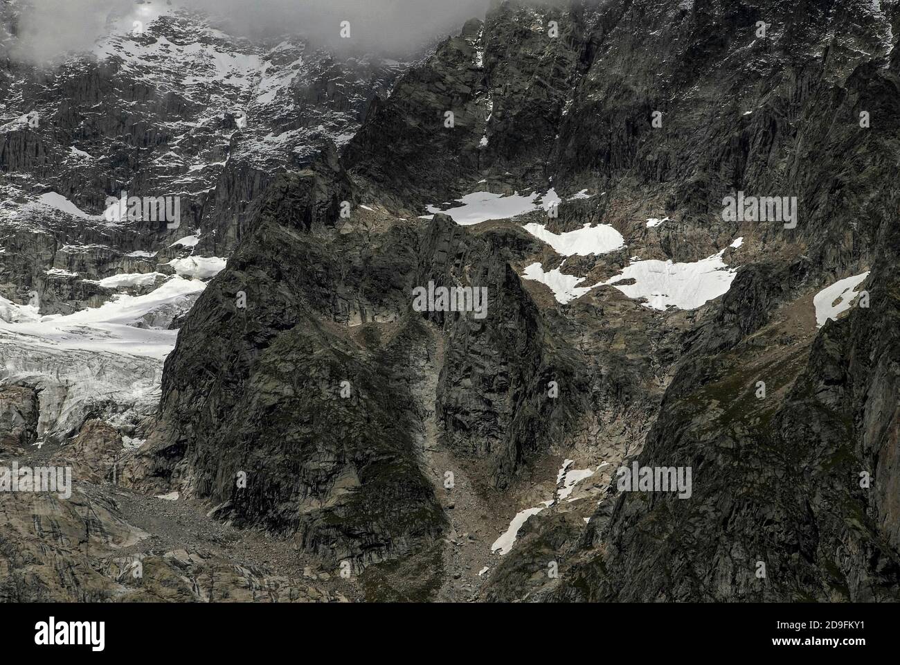 Im August, Monate vor dem Beginn des alpinen Winters, bleiben in den Mulden in der Nähe der großen Gletscher, die sich an den zerklüfteten Hängen des Mont Blanc / Monte Bianco-Massivs abschneien, nur wenige Stellen verschneit. Während die schroffe Burg-ähnliche Formation in der Mitte dieses Blickes fast frei von Schnee und Eis ist. Aufnahme aus der Nähe von Entrèves, Courmayeur, Aostatal, Italien, in der Nähe des italienischen Eingangs zum 11.6 km (7.25 m) Mont-Blanc-Tunnel, der seit 1965 eine Alpenstraßenverbindung nach Frankreich bietet. Stockfoto