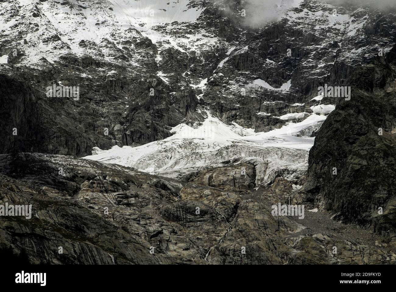 Im August, Monate vor dem Beginn des alpinen Winters, stürzt Schmelzwasser in den gestreift Felsen unter den Höhenschneefeldern und am Ende der Gletscher, die die zerklüfteten Hänge des Mont Blanc / Monte Bianco-Massivs hinunterschnappen, in Kanäle und Spalten. Aufnahme aus der Nähe von Entrèves, Courmayeur, Aostatal, Italien, in der Nähe des italienischen Eingangs zum 11.6 km (7.25 m) Mont-Blanc-Tunnel, der seit 1965 eine Alpenstraßenverbindung nach Frankreich bietet. Stockfoto