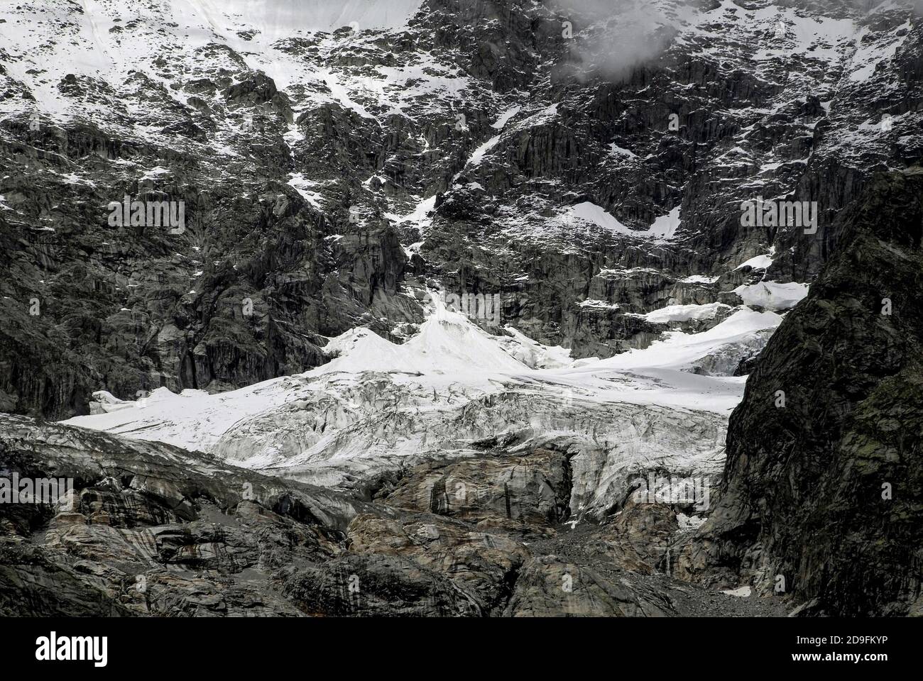 Im August, Monate vor dem Beginn des alpinen Winters, stürzt Schmelzwasser in den gestreift Felsen unter den Höhenschneefeldern und am Ende der Gletscher, die die zerklüfteten Hänge des Mont Blanc / Monte Bianco-Massivs hinunterschnappen, in Kanäle und Spalten. Aufnahme aus der Nähe von Entrèves, Courmayeur, Aostatal, Italien, in der Nähe des italienischen Eingangs zum 11.6 km (7.25 m) Mont-Blanc-Tunnel, der seit 1965 eine Alpenstraßenverbindung nach Frankreich bietet. Stockfoto
