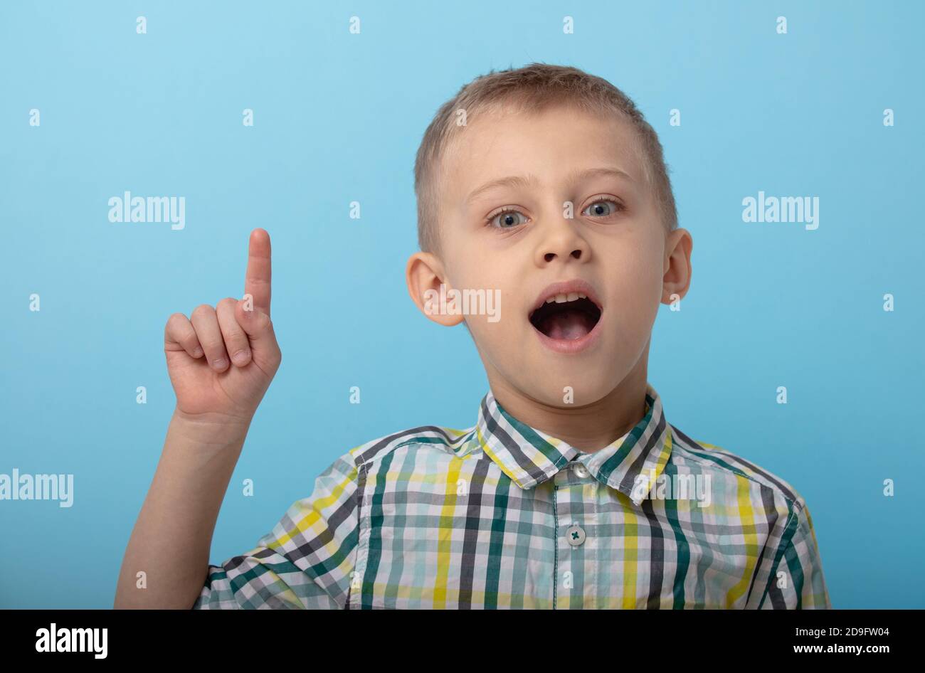 Ein Junge in einem karierten Hemd posiert auf blauem Hintergrund. Das Kind zeigt Emotionen an der Kamera. Konzept der Ausbildung und Vorbereitung auf die Schule Stockfoto