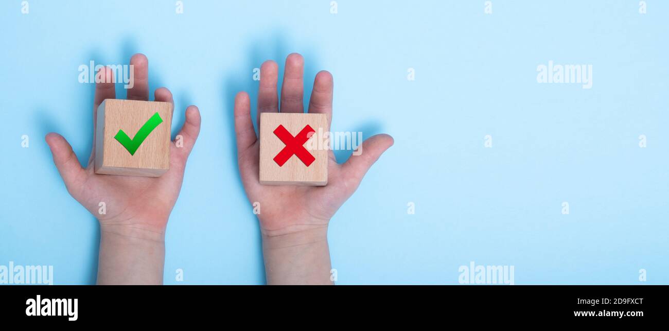 Nahaufnahme einer Hand, die zwei Holzklötze auf einem blauen Hintergrund platziert. True und false Symbole akzeptieren zur Auswertung abgelehnt, Ja oder Nein auf Holzblöcken ein Stockfoto