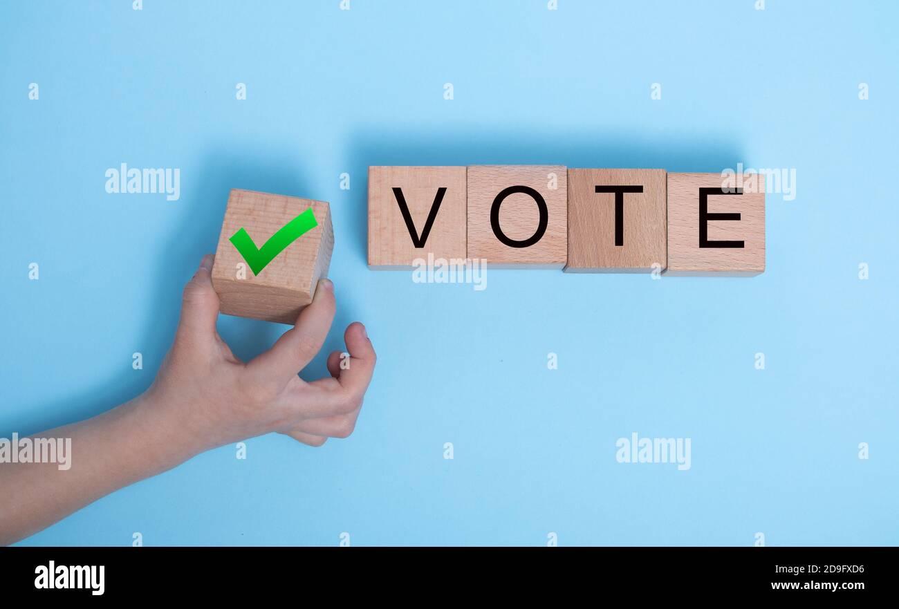 Die Worte STIMMEN über Holzwürfel ab. Das Konzept der Wahl der richtigen Lösung. Die Hand des Kindes hält einen Block, trifft eine Wahl, stimmt für die richtige Entscheidung Stockfoto