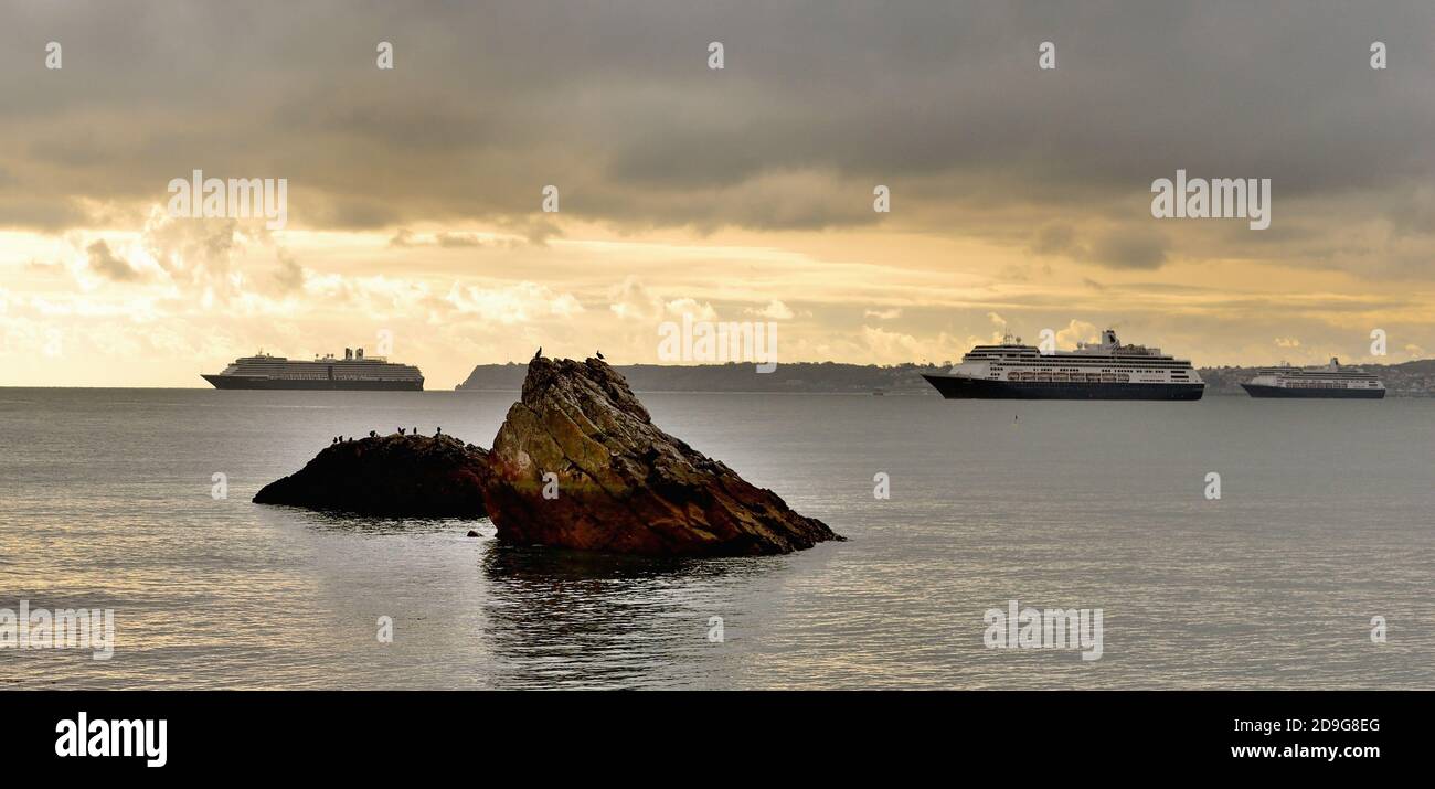 Kreuzfahrtschiffe vor Anker in Tor Bay während der Coronavirus-Pandemie, unter bedrohlichem Himmel. Stockfoto