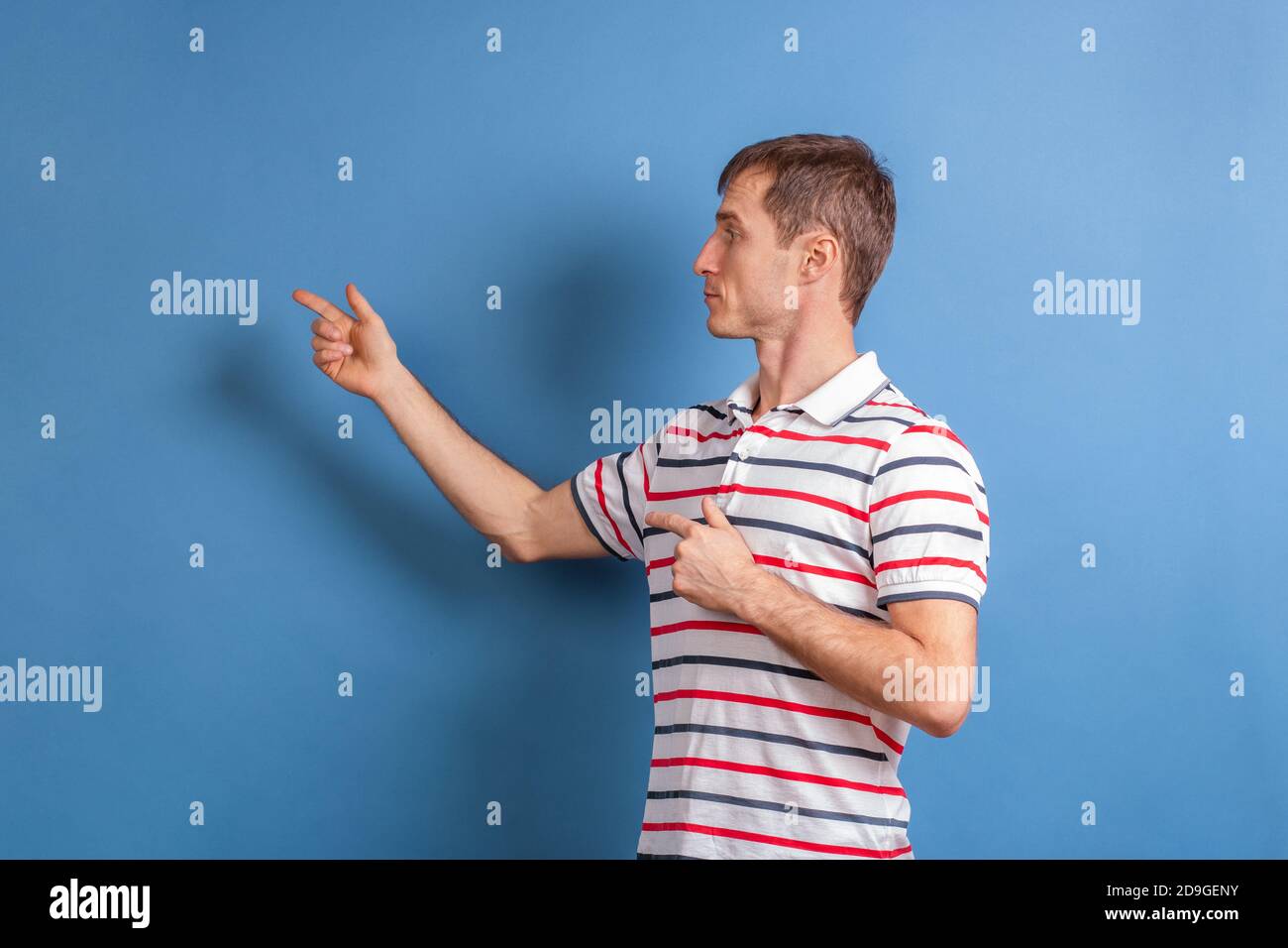 Männlicher Lehrer zeigt etwas an der Wand auf einem blauen Hintergrund. Der junge Mann zeigt mit dem Finger auf den Werbetext. Stockfoto