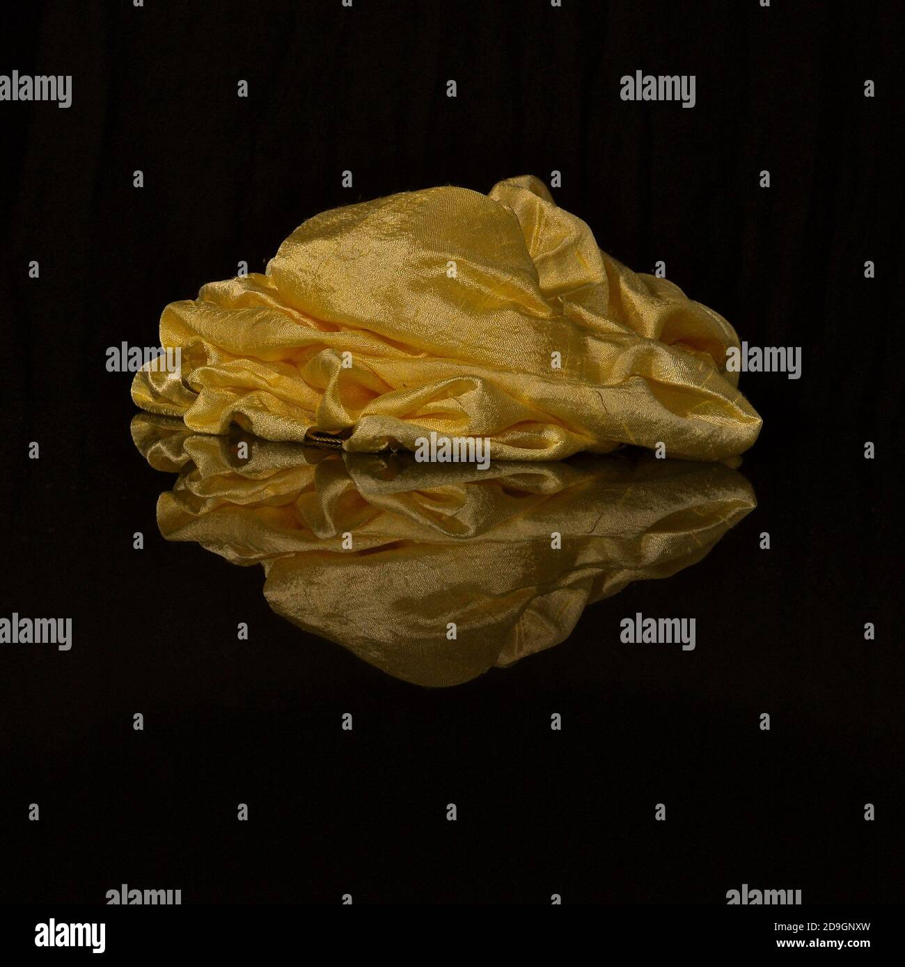 Ein gelber Seidenschal auf einer glänzenden schwarzen reflektierenden Oberfläche, die ein invertiertes Spiegelbild zeigt. Stockfoto