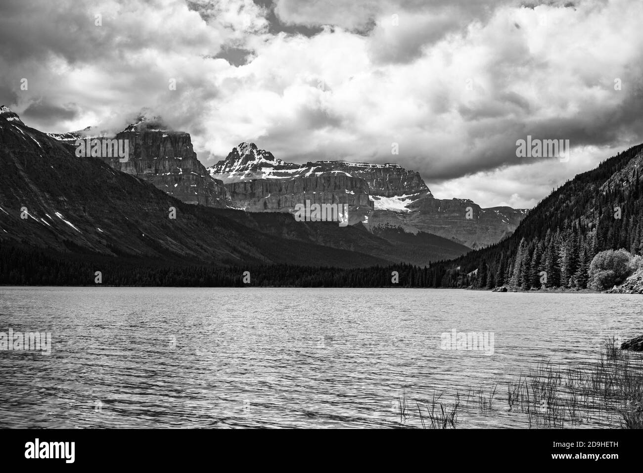 Graustufenaufnahme eines Sees umgeben von Bergen auf einem wolkiger Tag Stockfoto