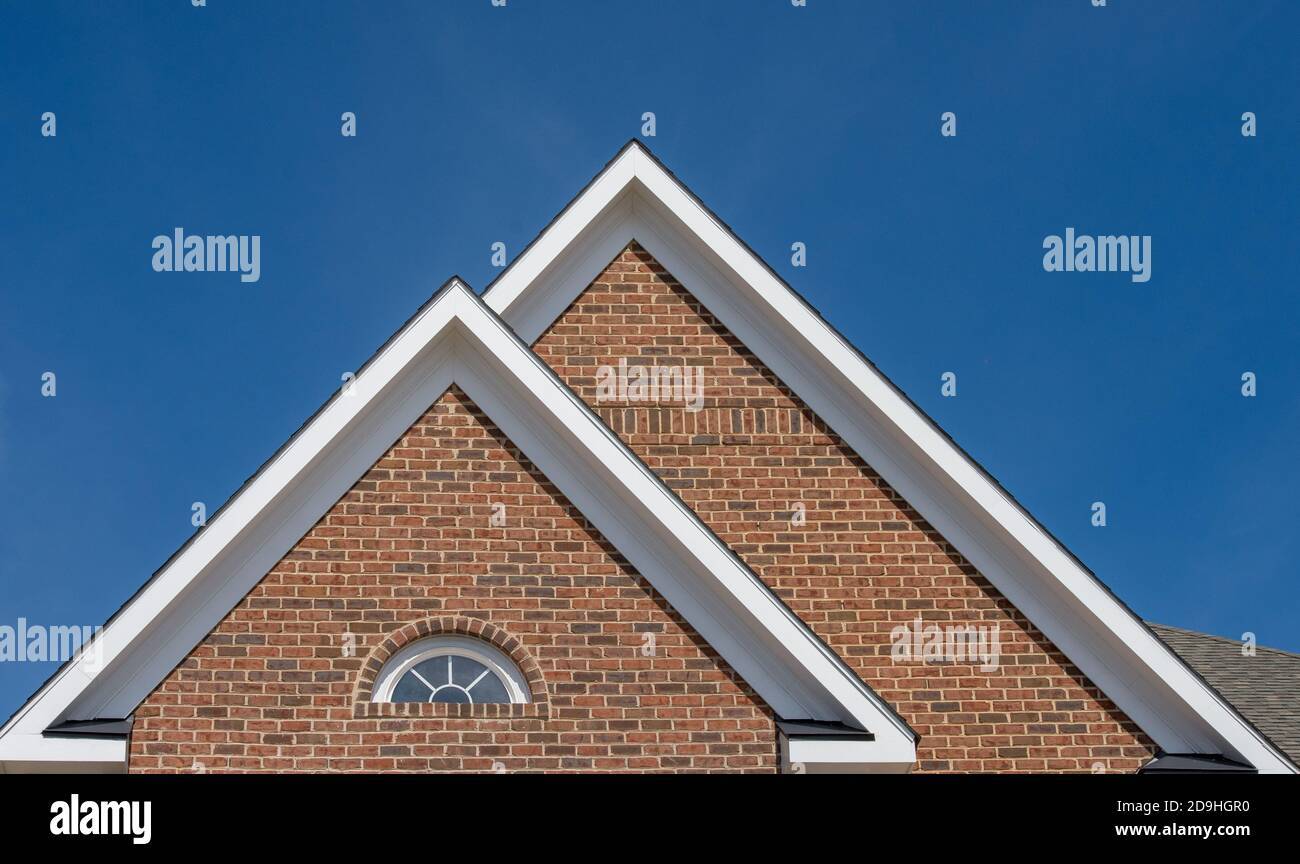 Einzel- und Doppelkiebel-Dächer mit Backstein- oder Vinylgleitviereck und ovalen Dachfenstern mit blauem, neutralem Himmel-Hintergrund Stockfoto