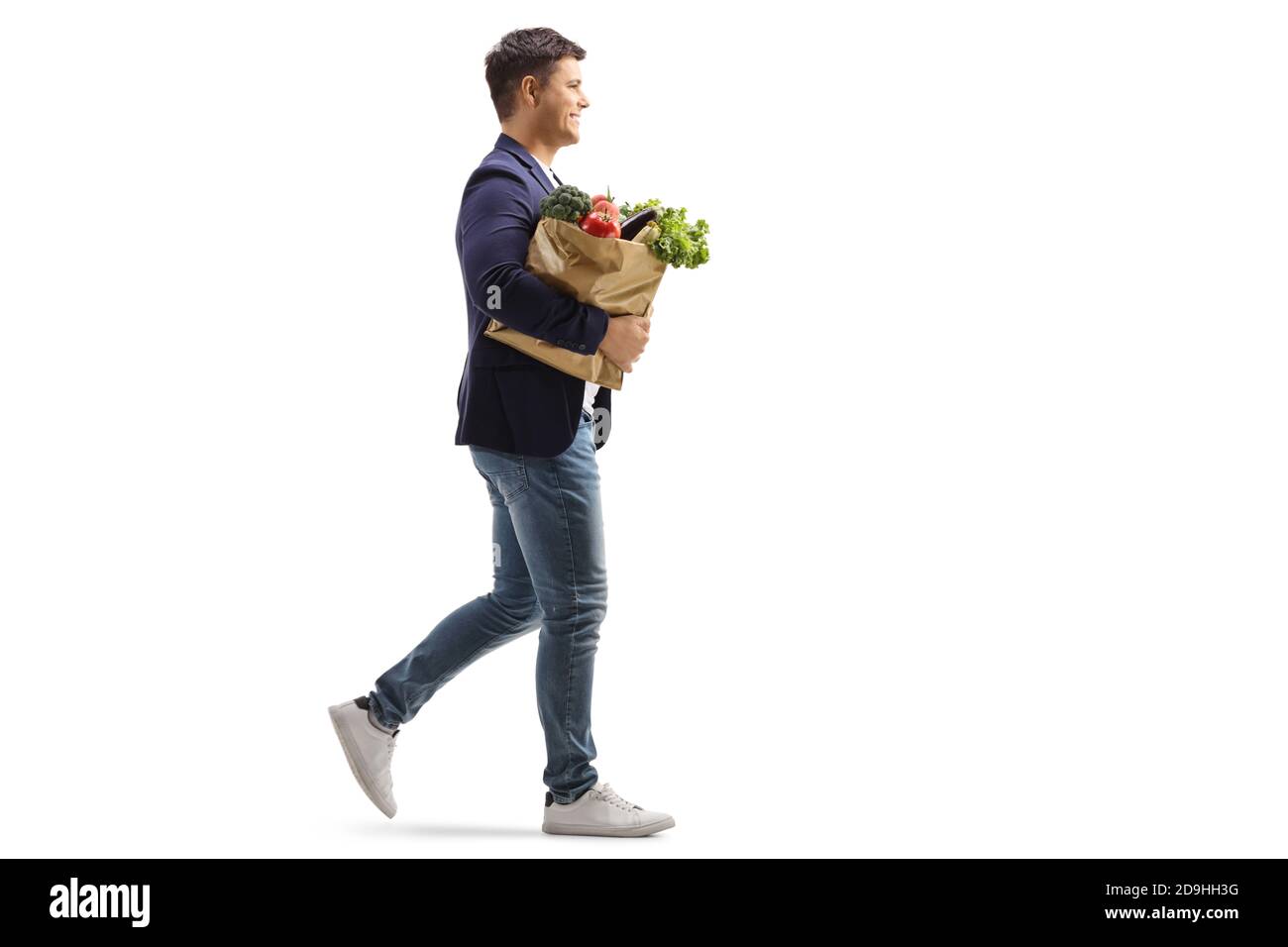 In voller Länge Profilaufnahme eines lächelnden jungen Mannes beim Gehen Und eine Papiertasche mit Lebensmitteln isoliert auf weiß Hintergrund Stockfoto