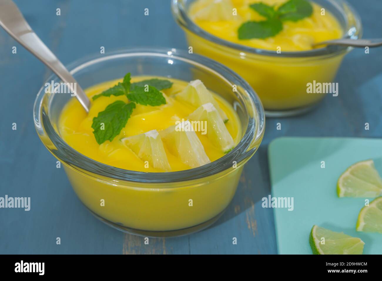 Zitronenpudding oder Zitronenquark in Glasschüsseln mit Minzblättern und Zitronenscheiben auf blauem Holzhintergrund serviert, süße Sahne, leckerer Desser Stockfoto