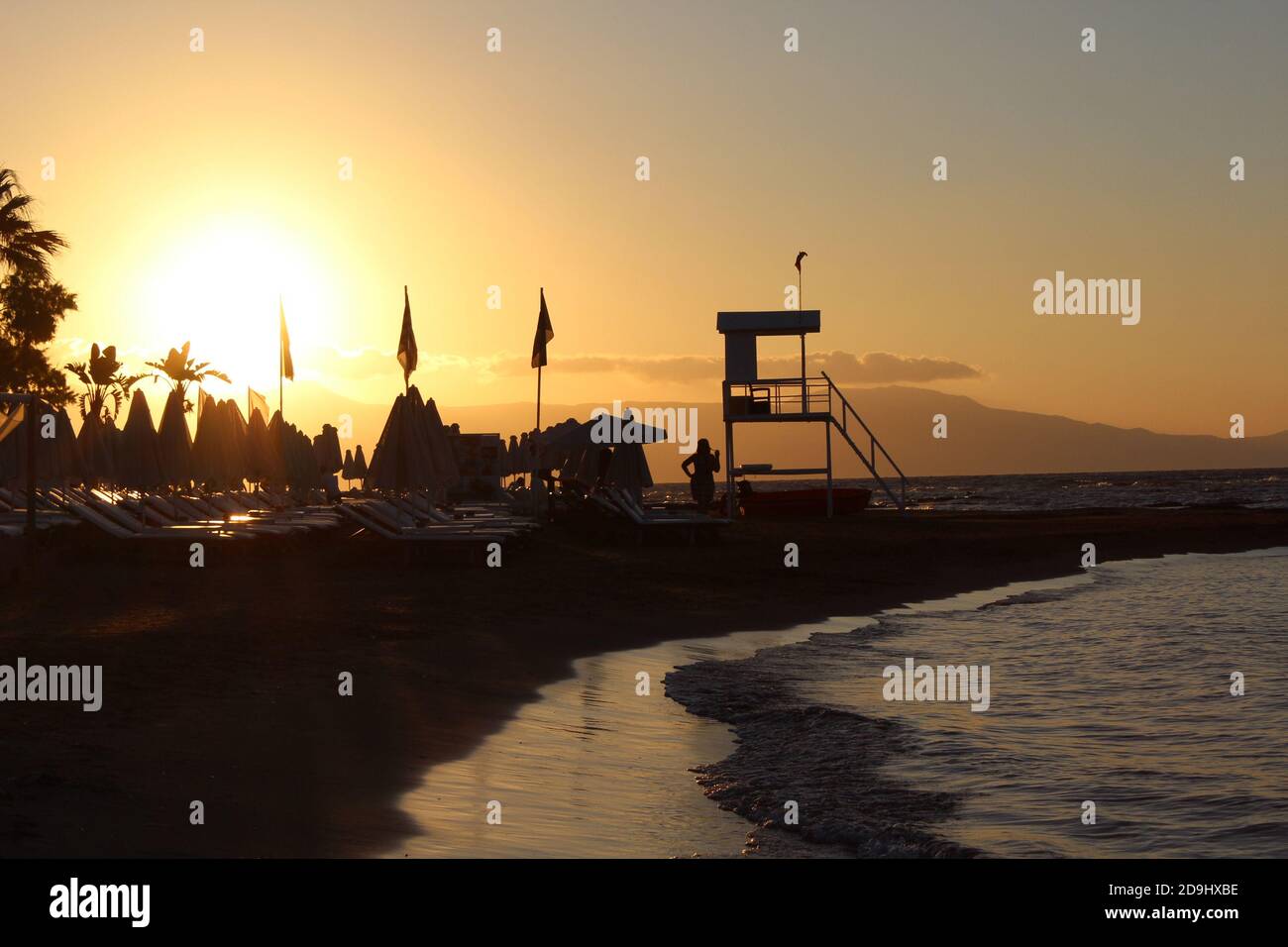 Sonnenuntergang am Strand in Griechenland, Silhouette einer Frau und ein Wachturm Stockfoto