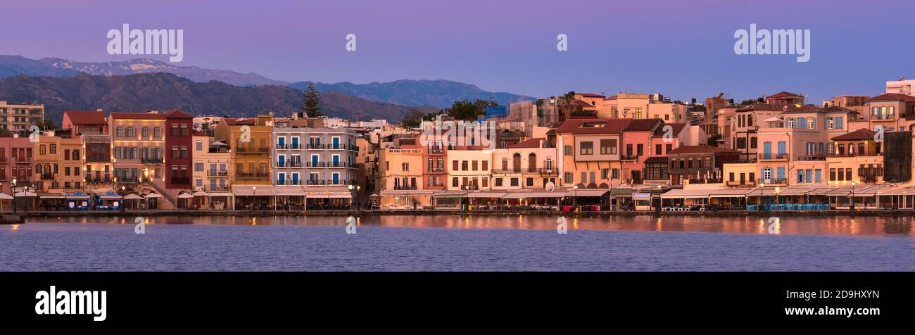 Sonnenaufgang oder Sonnenuntergang über dem alten venezianischen Hafen und der Hafenpromenade von Chania, Kreta, Griechenland. Großer purpurner Himmel, entfernte kretische Berge. Panoramaaufnahme. Stockfoto
