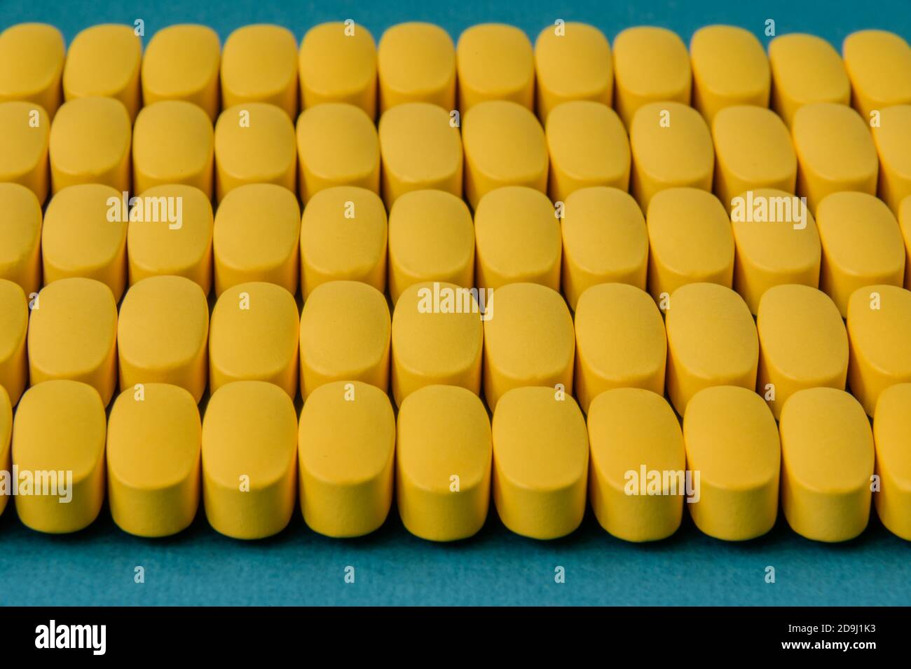 Reihen von vielen gelben Pillen Tabletten Vitamin auf blauer Oberfläche Stockfoto