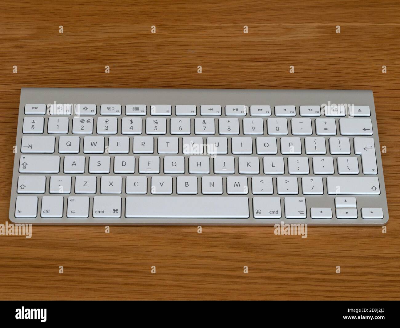 Apple Magic kabelloser Bluetooth-Computer GB englische QWERTY-Tastatur mit weißen Tasten und silberfarbenem eloxiertem Aluminiumgehäuse auf Holzhintergrund. Stockfoto