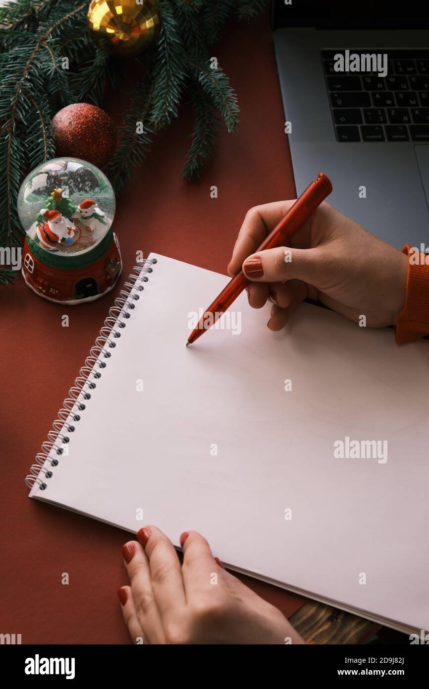 Frau im Heimbüro schreibt einen Brief an den Weihnachtsmann an Weihnachten. Schneekugel und Laptop in der Nähe Stockfoto