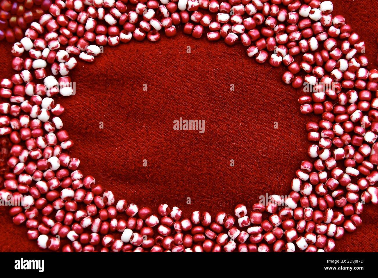 Makro-Bild von kleinen Glasperlen auf einem roten Stoff in einer ovalen Rahmenform genäht. Stockfoto