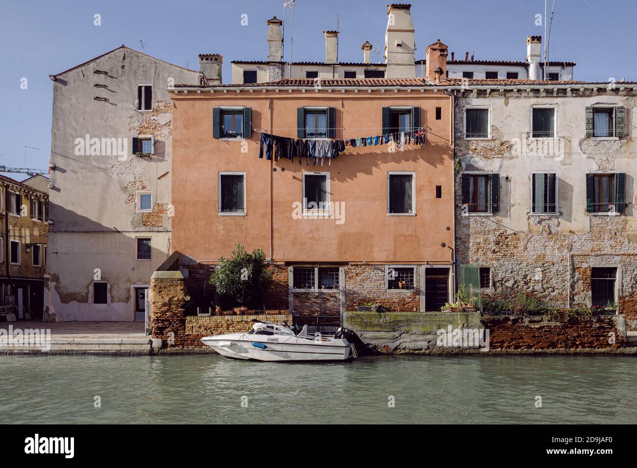 Hohe Außenfassade mit orangefarbener Wand, festgefestertes Boot auf einem Venedig-Kanal Stockfoto