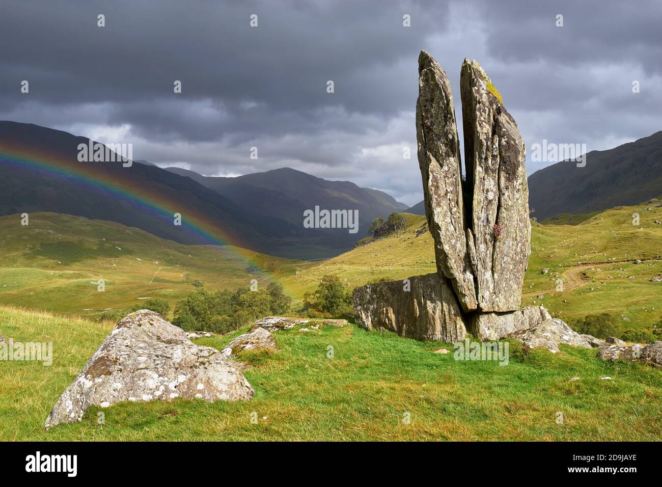 Ein gespaltener aufrechter Stein in Gleun Dà-Eigg, Glen Lyon, bekannt als die betenden Hände von Mary oder Fionn's Rock, Perth und Kinross, Schottland. Mit Regenbogen. Stockfoto