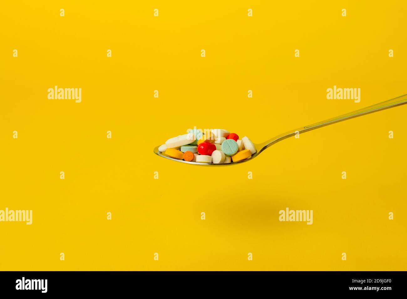 Löffel voller Pillen auf gelbem Hintergrund. Selbstmedikation und Drogenmissbrauch Konzept. Stockfoto