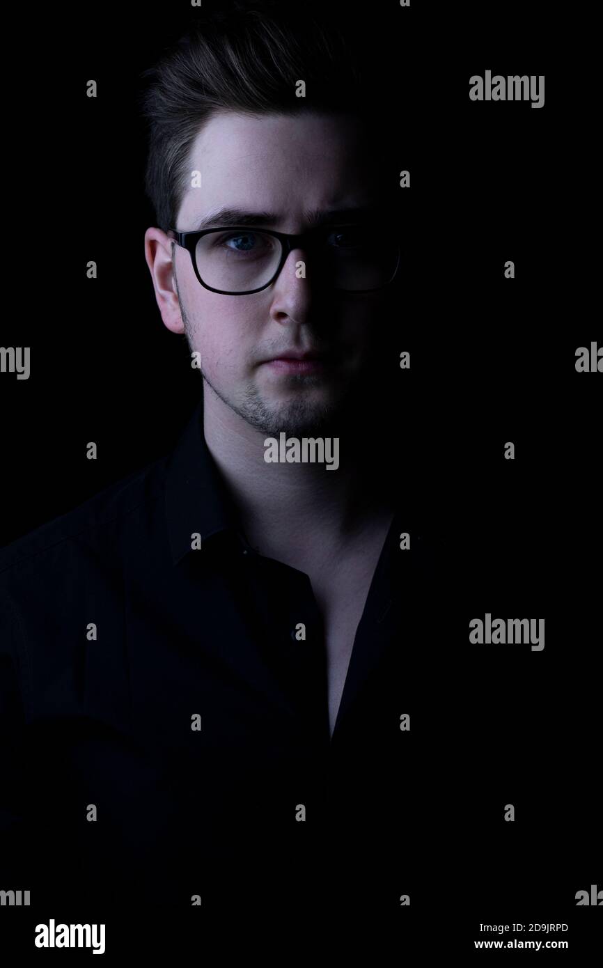 Weißer Mann starrt vor schwarzem Hintergrund in die Kamera. Stockfoto