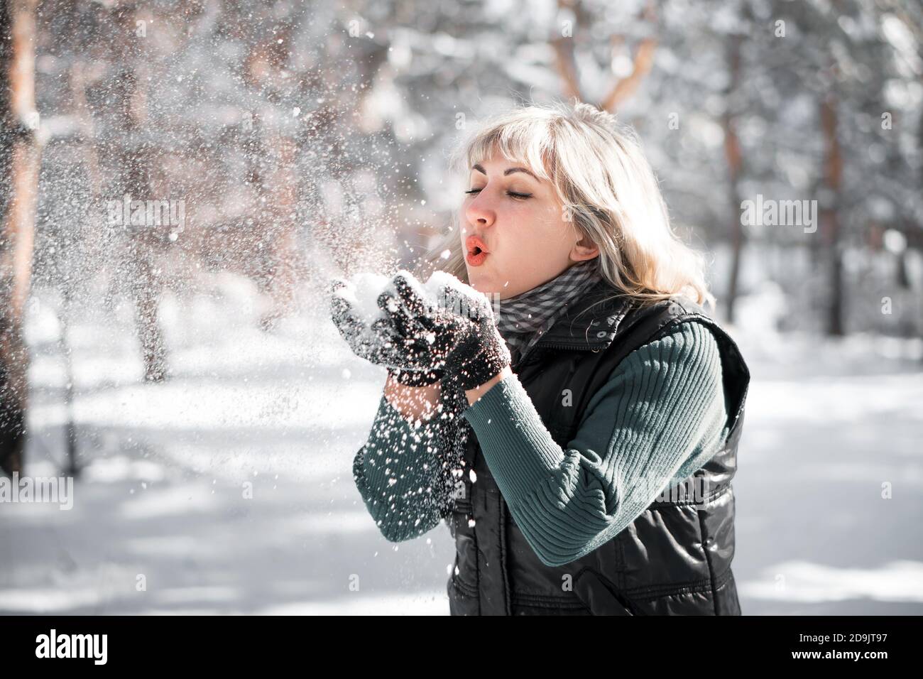 Erwachsene Frau bläst auf Schneeflocken in ihren Händen. Winterurlaub im Wald. Stockfoto