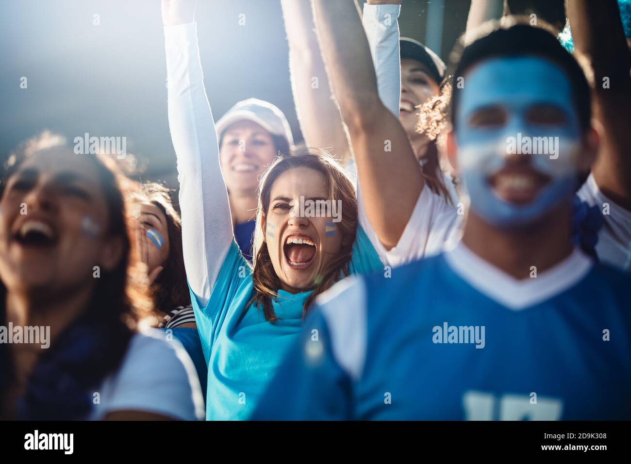 Argentinische Frau mit einer Gruppe jubelender Fußballfans im Stadion. Eine Menge Fußballfans jubeln ihrem Team bei einem Spiel im Stadion zu. Stockfoto
