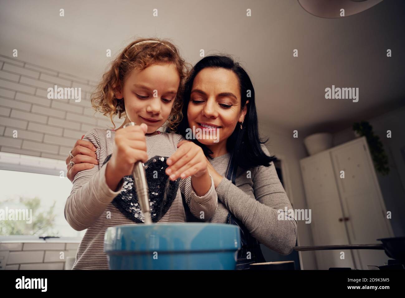 Low-Angle-Ansicht von Mutter und Tochter Schnurren Teig in Schüssel und Zugabe von Gewürzen in der Schüssel während des Kochens in der Küche Stockfoto