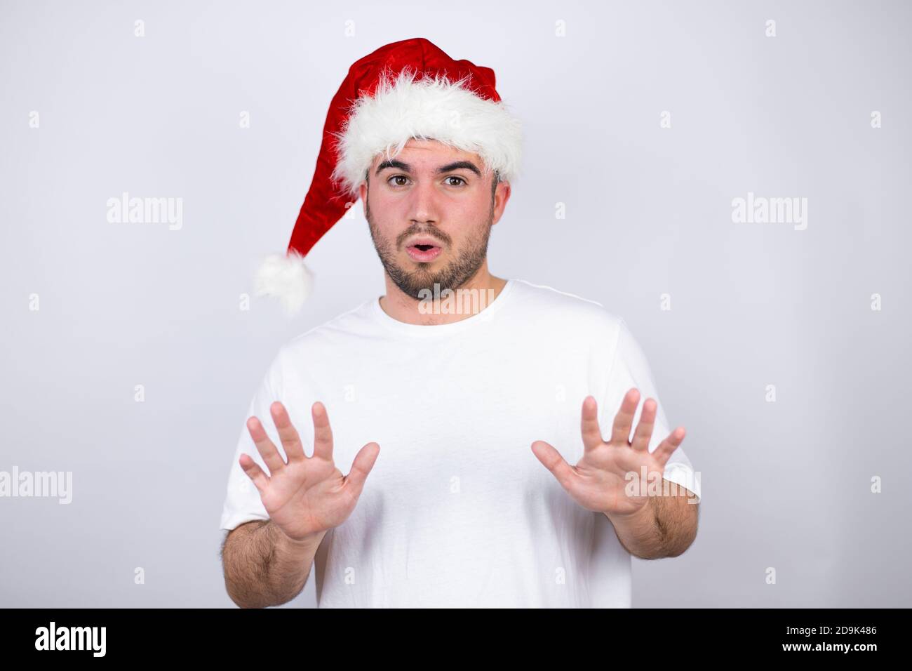 Junger schöner Mann trägt einen Weihnachtsmann Hut über weißem Hintergrund Angst und erschrocken vor Angst Ausdruck Stop-Geste mit Händen, schreien im Schock. Schwenken Stockfoto