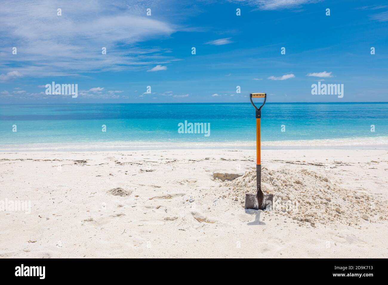 Schaufel in Sand am Strand. Weitwinkelbild einer Schaufel im Sand am Strand unter einem teilweise bewölkten blauen Himmel. Stockfoto