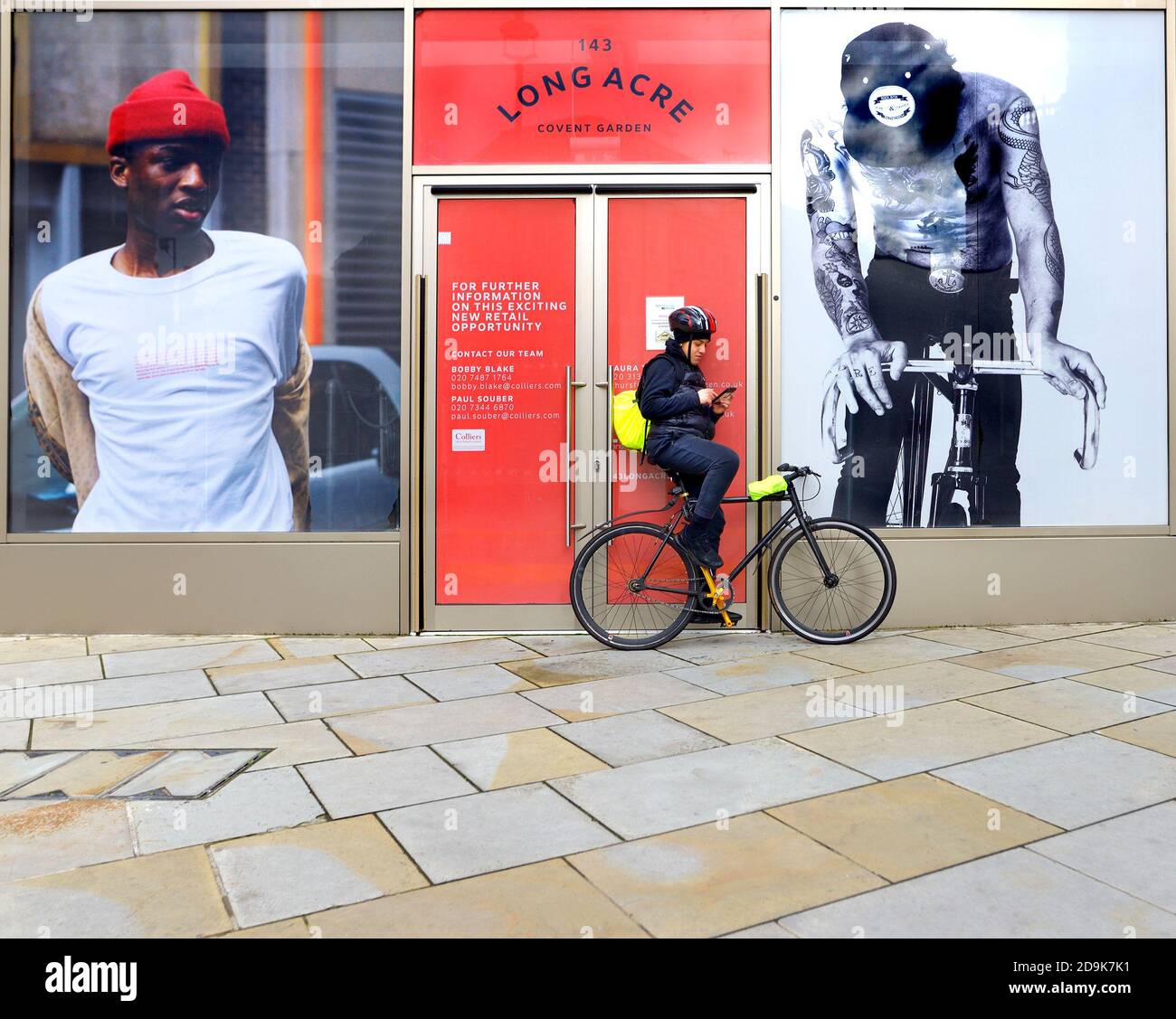 London, England, Großbritannien. Junger Mann, der sich in Long Acre, Covent Garden, auf seinem Fahrrad ausruhte und sein Handy überprüfte Stockfoto