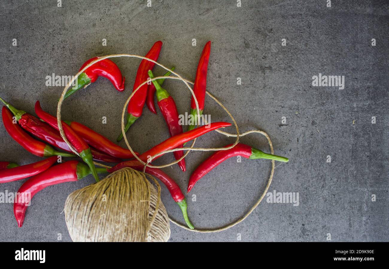 Rote Chilischoten Girlande machen. Frische Paprika und Leinenseil auf dunkelgrauem Tisch. Foto von oben mit Kopierbereich. Handgemachte Wohndekorationen. Stockfoto