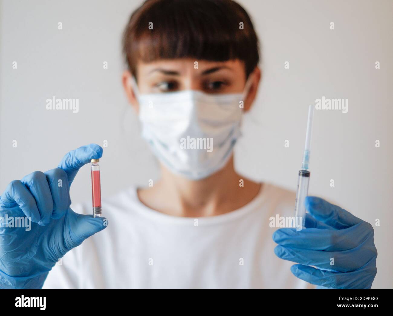 Arzt Krankenschwester Frau trägt Schutzmaske und Handschuhe - hält Flasche Impfstoff Medizin und Spritze Stockfoto